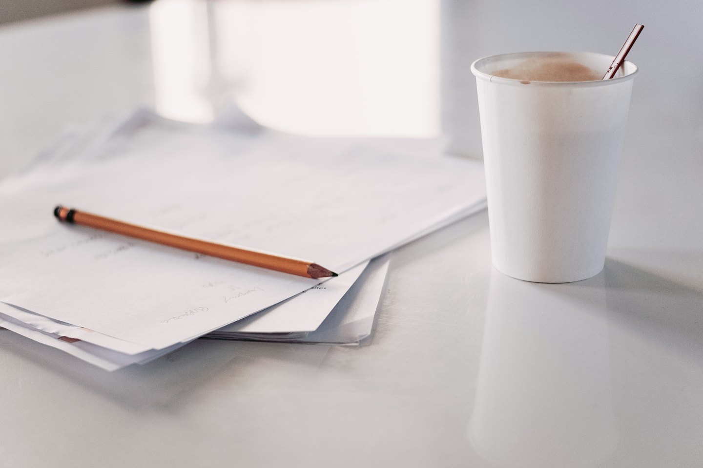 A pencil sits on a stack of papers next to a coffee cup.