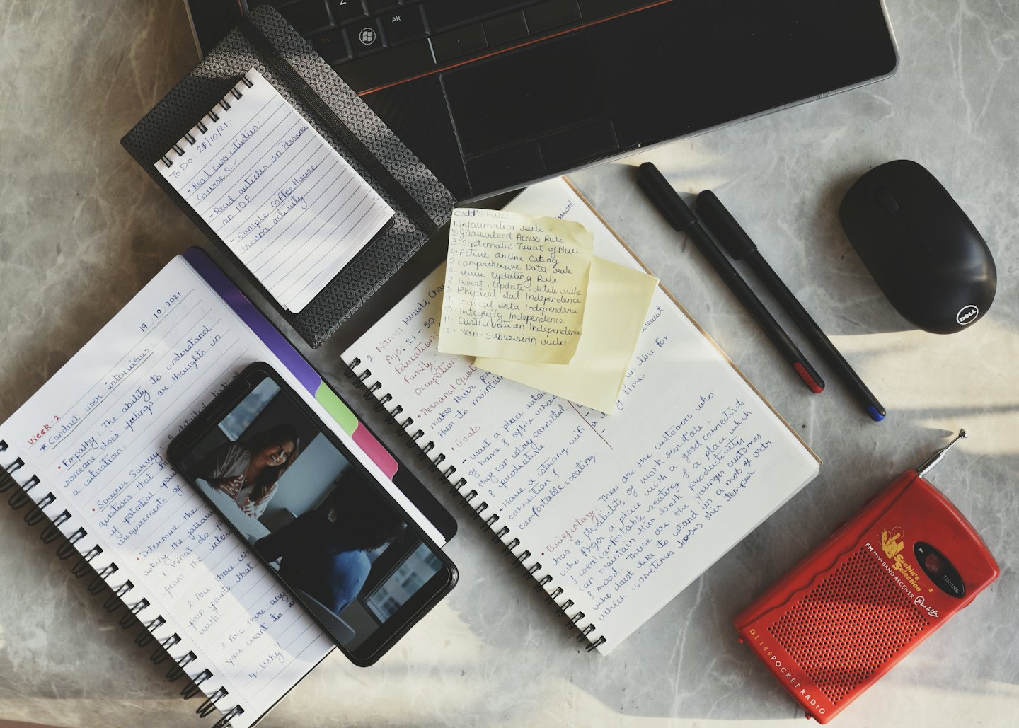 Overhead view of a busy desk with notebooks, laptop, and sticky notes.
