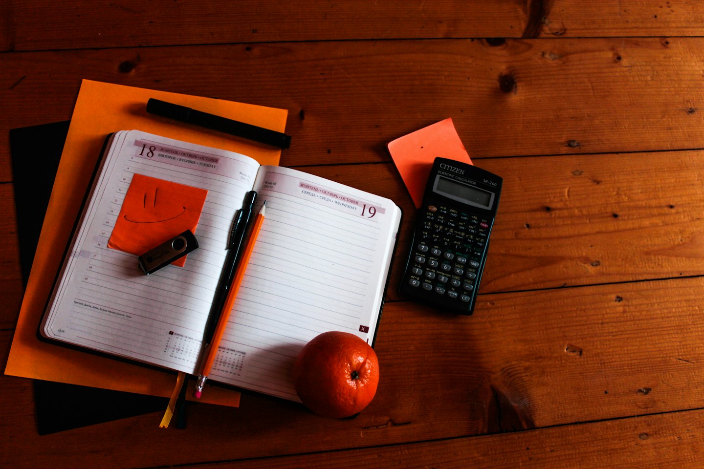 Planner, calculator, pens, and orange items on a desk.